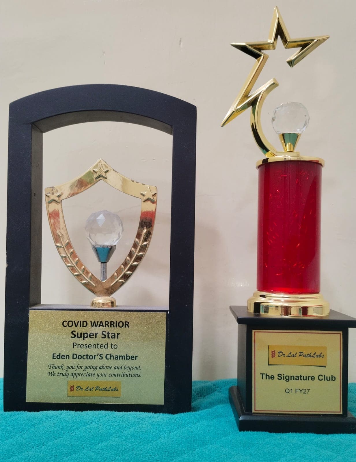 Two trophies from Dr. Lal PathLabs: a COVID Warrior Super Star plaque presented to Eden Doctor's Chamber, and a gold star trophy for The Signature Club, Q1 FY27